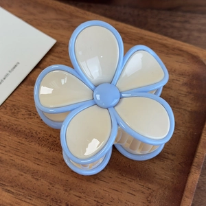 Détail de la pince à cheveux fleur bleue et crème sur plateau en bois noir