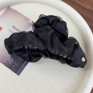 Detailed texture of black pleated organza fabric on hair claw with gold charm detail
