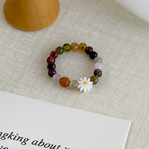 Close-up of a colorful beaded daisy ring on a soft linen textured background
