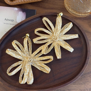 Bohemian woven raffia flower earrings with gold metal stud in a rustic wooden display