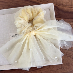 Détail d'un chouchou en tulle jaune clair avec perles blanches et grand nœud élégant