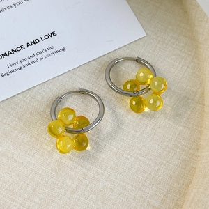 Detailed close-up of silver hoop earrings with yellow translucent beads on elegant background