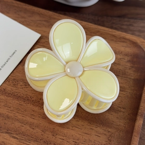 Détail de la pince à cheveux fleur jaune et crème sur un plateau en bois foncé