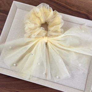Détail du chouchou en maille jaune clair avec de longs rubans et des perles blanches