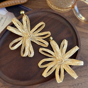 Bohemian woven raffia flower earrings with golden metallic stud on wooden tray