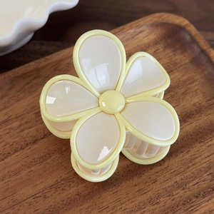 Détail d'une pince à cheveux en forme de fleur crème brillante sur un plateau en bois