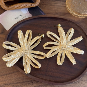Detailed macro view of woven raffia flower earrings with golden studs on wooden tray