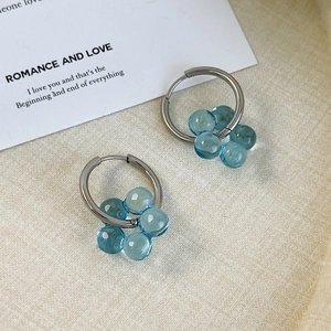 Detail view of blue beaded flower earrings with silver hoops on a textured tray