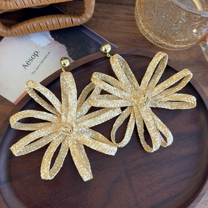 Macro shot of oversized woven straw flower earrings with a polished gold stud detail