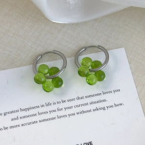 Detail of silver hoop earrings with green translucent flower pendants on white paper
