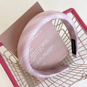 Close-up of light pink striped fabric headband featuring a woven HAND MADE detail tag