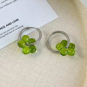 Macro shot of silver hoop earrings with green flower bead clusters on a tray