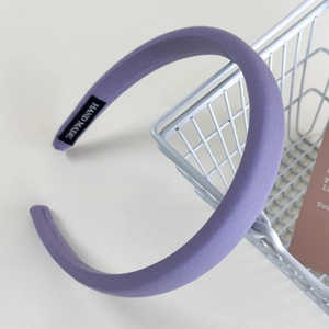 Dettaglio di un cerchietto in tessuto imbottito viola con etichetta nera fatta a mano