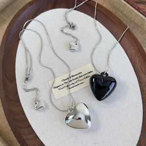 Silver snake chain necklace with black heart pendant on a rustic wooden tray