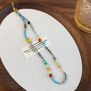 Ethnic bohemian beaded necklace with colorful stones and gold clasp on a wooden tray