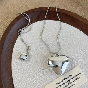 Close-up of polished silver heart pendant on a thin snake chain over wood decor