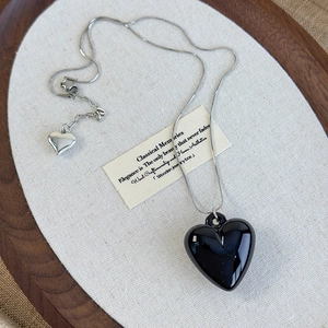 Detail view of silver snake chain necklace featuring a large black glossy heart pendant