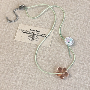 Detail of handmade beaded necklace with green cord and translucent brown flower pendant
