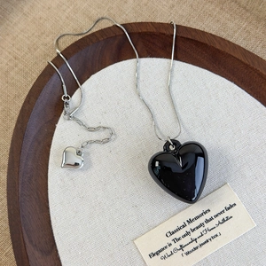 Detail of black glossy heart pendant on silver snake chain with small heart charm extension