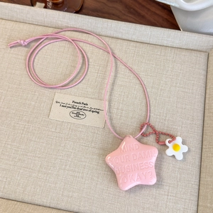 Vue détaillée du collier étoile rose avec texte gravé et breloque fleur sur un plateau
