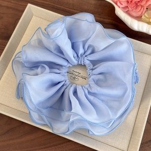 Détail d'un chouchou géant en mousseline bleu clair avec des plis sur un plateau chic