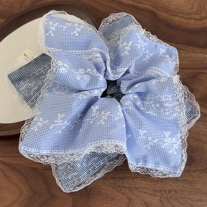 Light blue gingham scrunchie with white lace embroidery trim on a dark wooden background