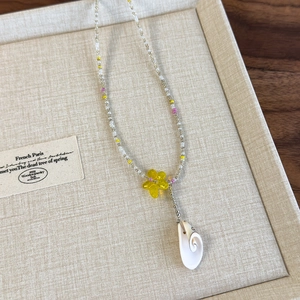 Close-up of handmade beaded necklace featuring yellow resin flower and shell pendant