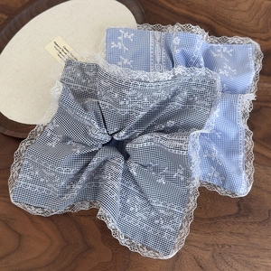 Detail of light blue and black plaid hair scrunchies with white lace edges on wood surface