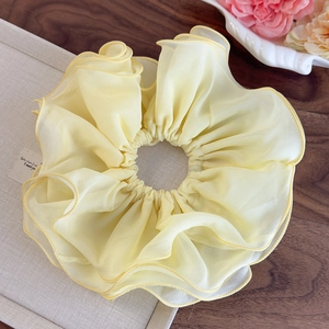 Détail d'un grand chouchou en mousseline jaune pâle avec volants sur boîte beige
