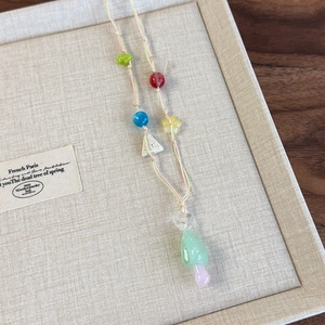 Detail of colorful beaded necklace with green glass mushroom pendant on textured box
