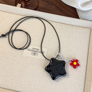 Détail macro du collier étoile noire avec texte et breloque fleur rouge pour femme