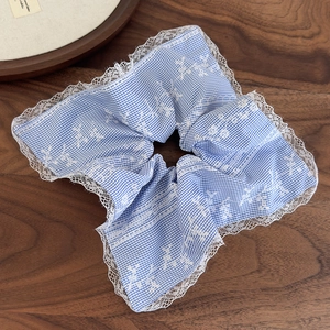 Detail of light blue gingham hair scrunchie with white lace edges and floral embroidery
