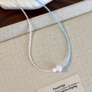 Detail of handmade beaded necklace with a small resin mushroom pendant on fabric background
