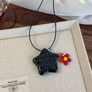 Gros plan du pendentif étoile noire avec lettrage en relief et petite fleur