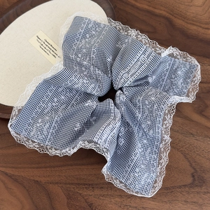 Close-up of black and white checkered scrunchie with white lace trim on wooden tray