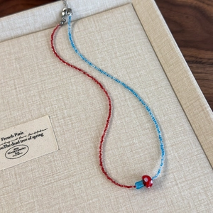 Detail of beaded necklace featuring red and blue beads with a cute mushroom pendant