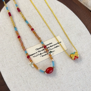 Close-up of colorful beaded necklace and gold snake chain with vintage pendant on a tray