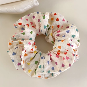 Détail d'un chouchou à imprimé cœurs colorés en coton texturé sur fond crème