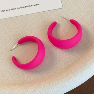 Dettaglio di orecchini a cerchio a C rosa neon opaco su una carta decorativa