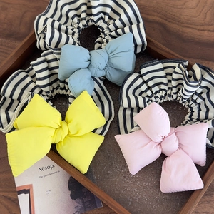 Detailed close-up of colorful bow scrunchies with striped elastic bands in a wooden tray
