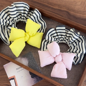 Close-up of yellow and pink striped bow scrunchies on a wooden tray with a card