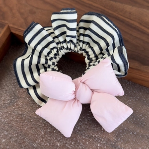 Close-up of black and white striped hair tie with a large fluffy pink bow on a wooden tray