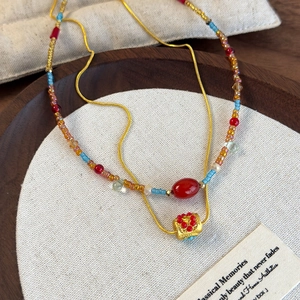 Close-up of colorful beaded necklace and gold chain on linen display within a wooden tray
