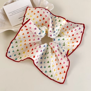Gros plan d'un chouchou blanc avec motifs cœurs arc-en-ciel et bordure rouge sur plateau