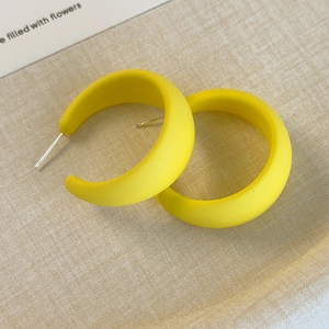 Dettaglio di orecchini a C in resina giallo opaco dal design moderno e minimalista