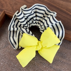 Close-up of a striped fabric scrunchie with a bright yellow bow on a wooden tray