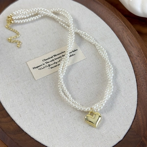 Gros plan détaillé du collier de perles à trois rangs avec pendentif cœur doré poli