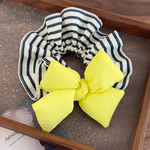 Close-up of a padded yellow bow on a black and white striped scrunchie over a glass tray