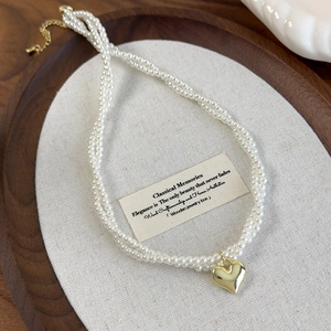 Gros plan d'un choker de perles à trois rangs avec pendentif cœur doré sur lin doux