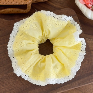 Detailed close-up of yellow and white lace scrunchie with floral embroidery on wood